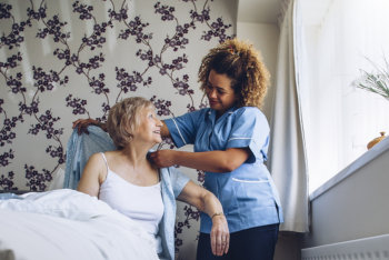 caregiver assists the elderly woman to dress up